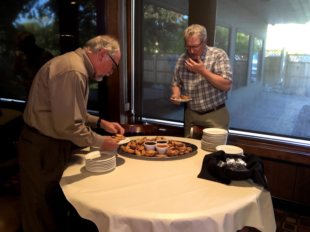 A group of men stand around a table with food on it

Description automatically generated with low confidence