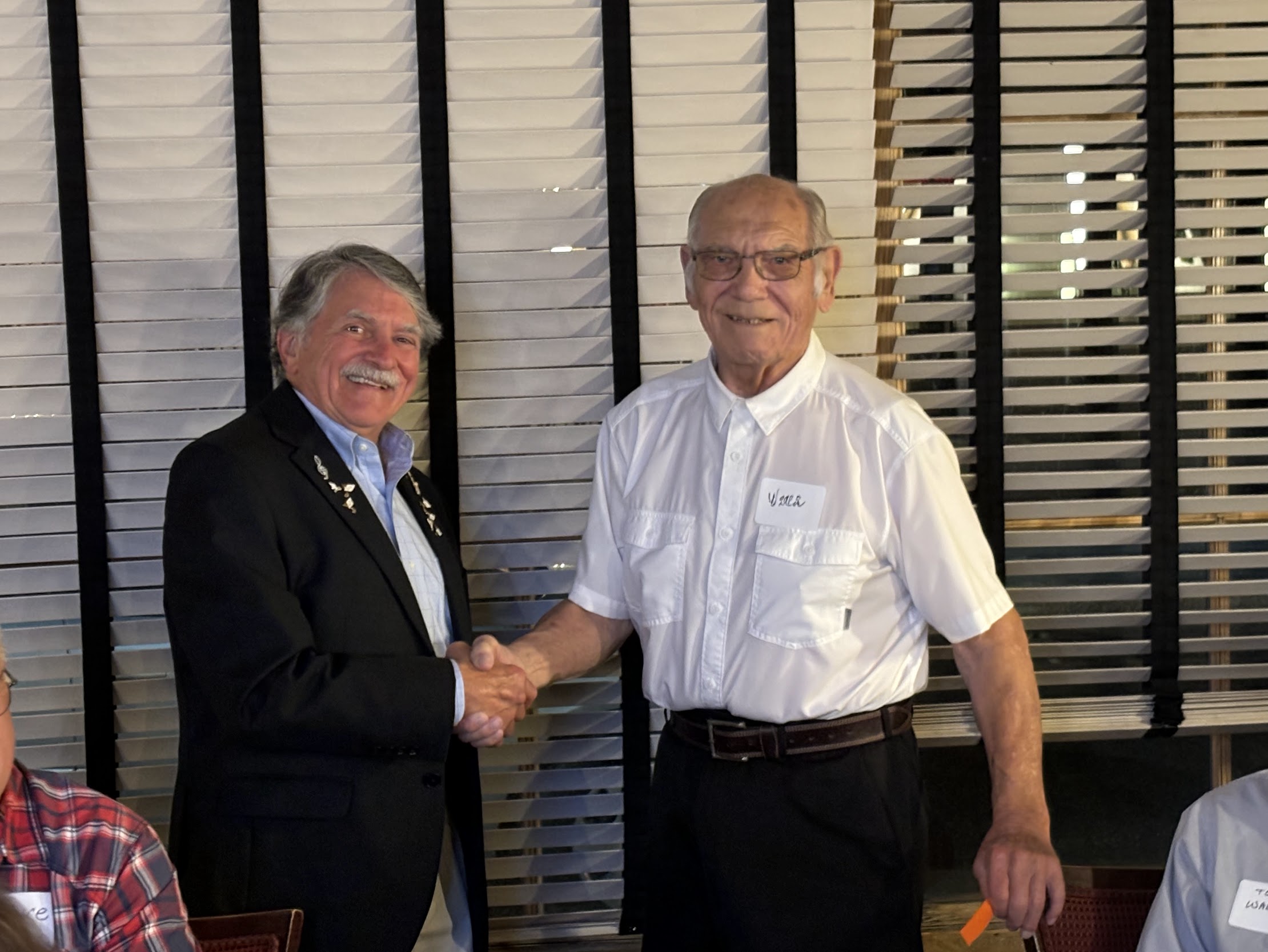 Two men shaking hands in front of a window

Description automatically generated