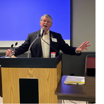 A person standing at a podium with his hand up
AI-generated content may be incorrect.